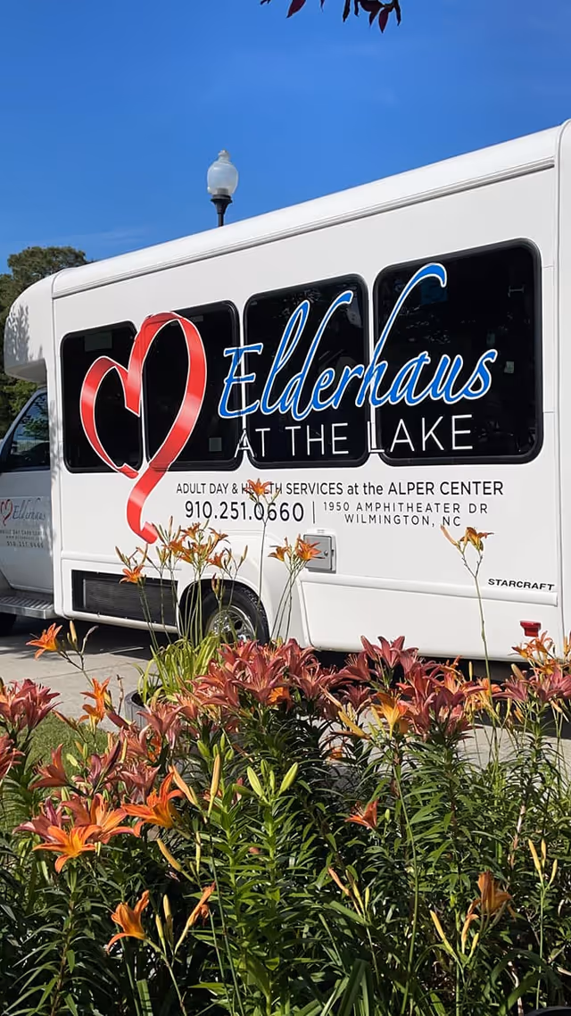 White Elderhaus at the Lake shuttle bus parked outdoors with orange lilies in the foreground.