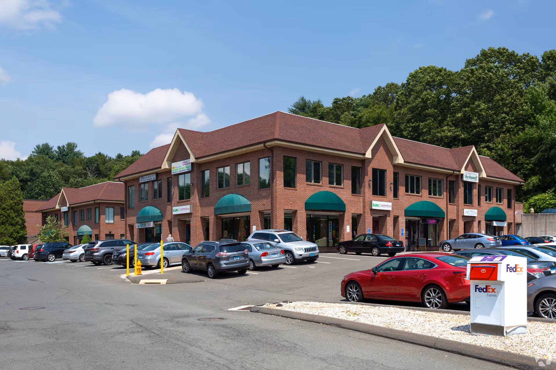 Brick building with green awnings, a parking lot, and a FedEx drop box in front.