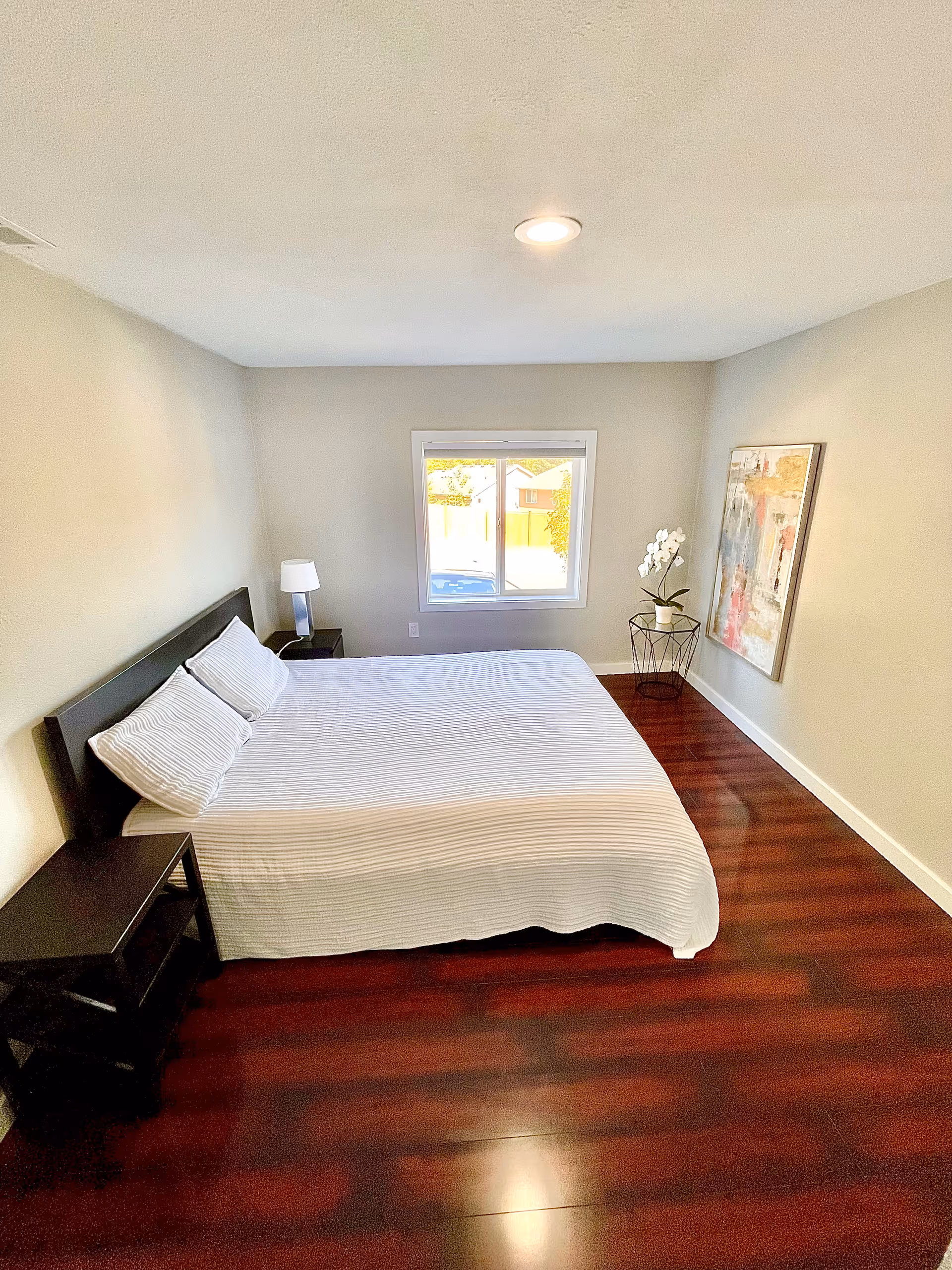 Cozy bedroom with a large bed, two nightstands, window, plant, and artwork.