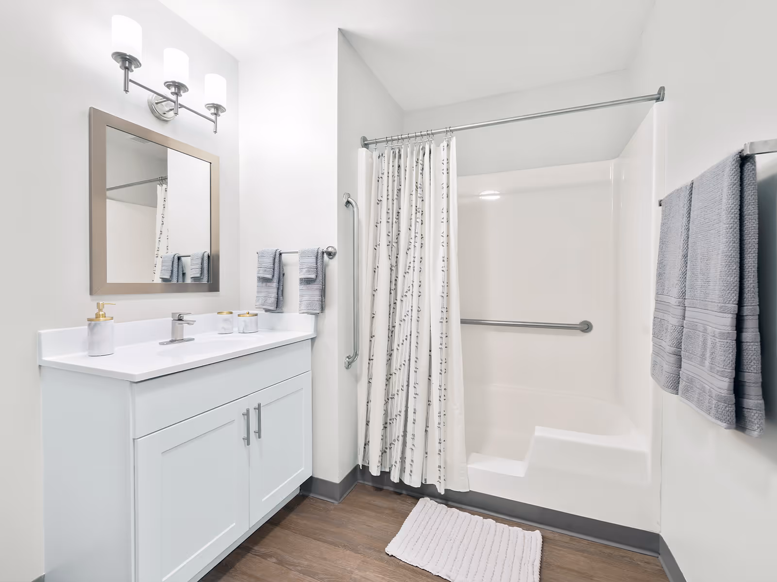 Modern bathroom with white vanity, mirror, towels, and a shower with a grab bar.