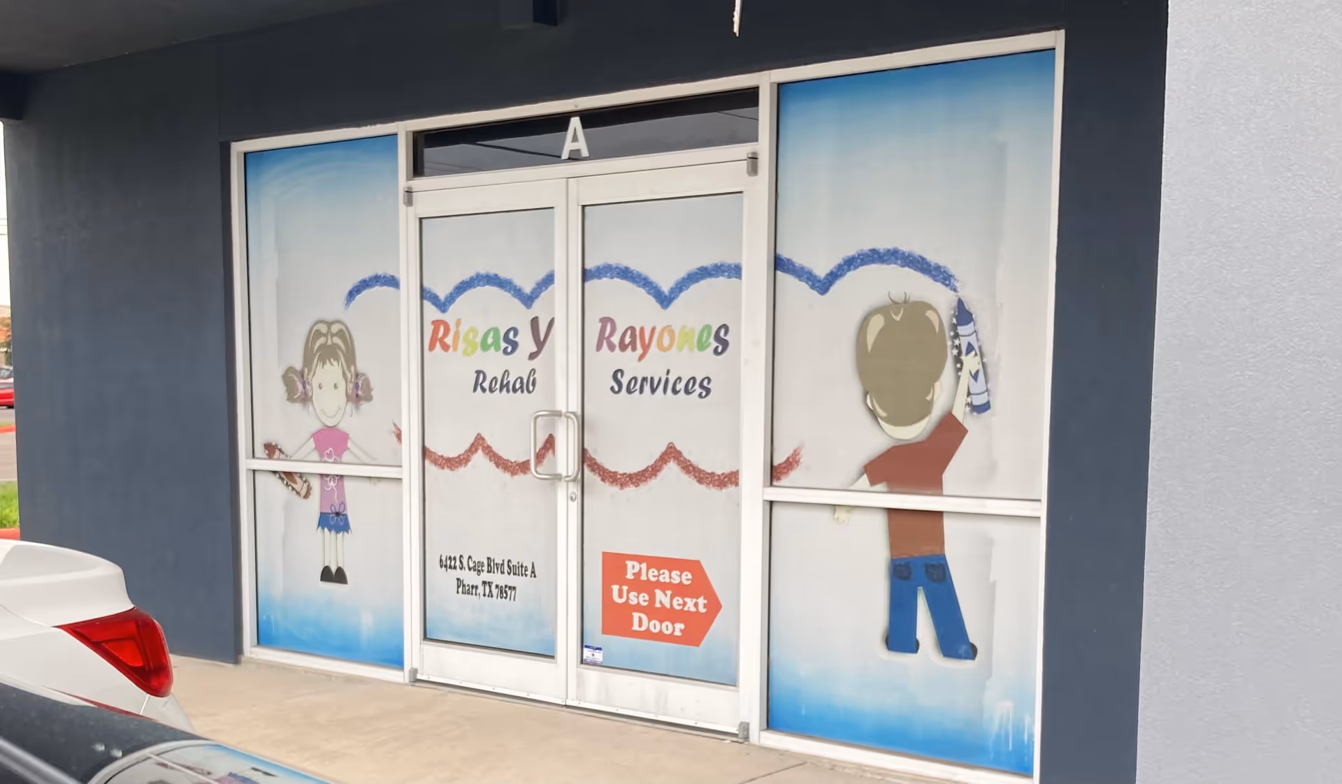 Glass front doors show 'Risas Y Rayones Rehab Services' with cartoon drawings.