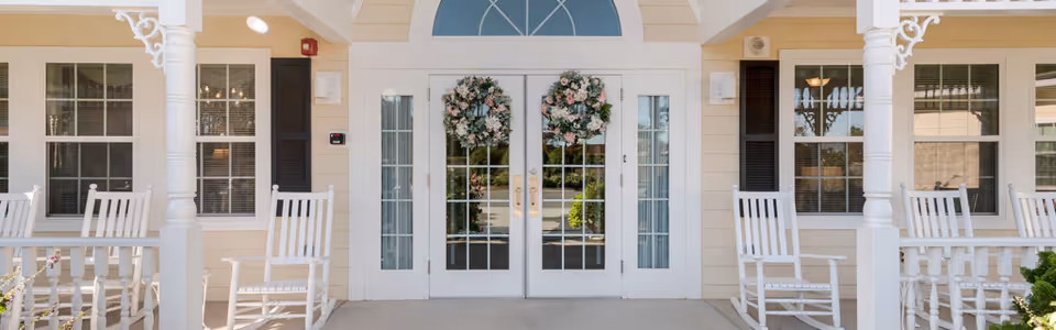 Front view of Cadence Senior Living Mint Hill entrance with white rocking chairs and wreaths