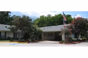 Single-story College Street Health Care Center exterior with entrance, trees, and flag.