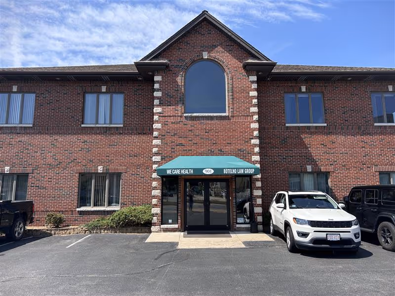 Brick building facade with arched window, glass doors, and parked cars.
