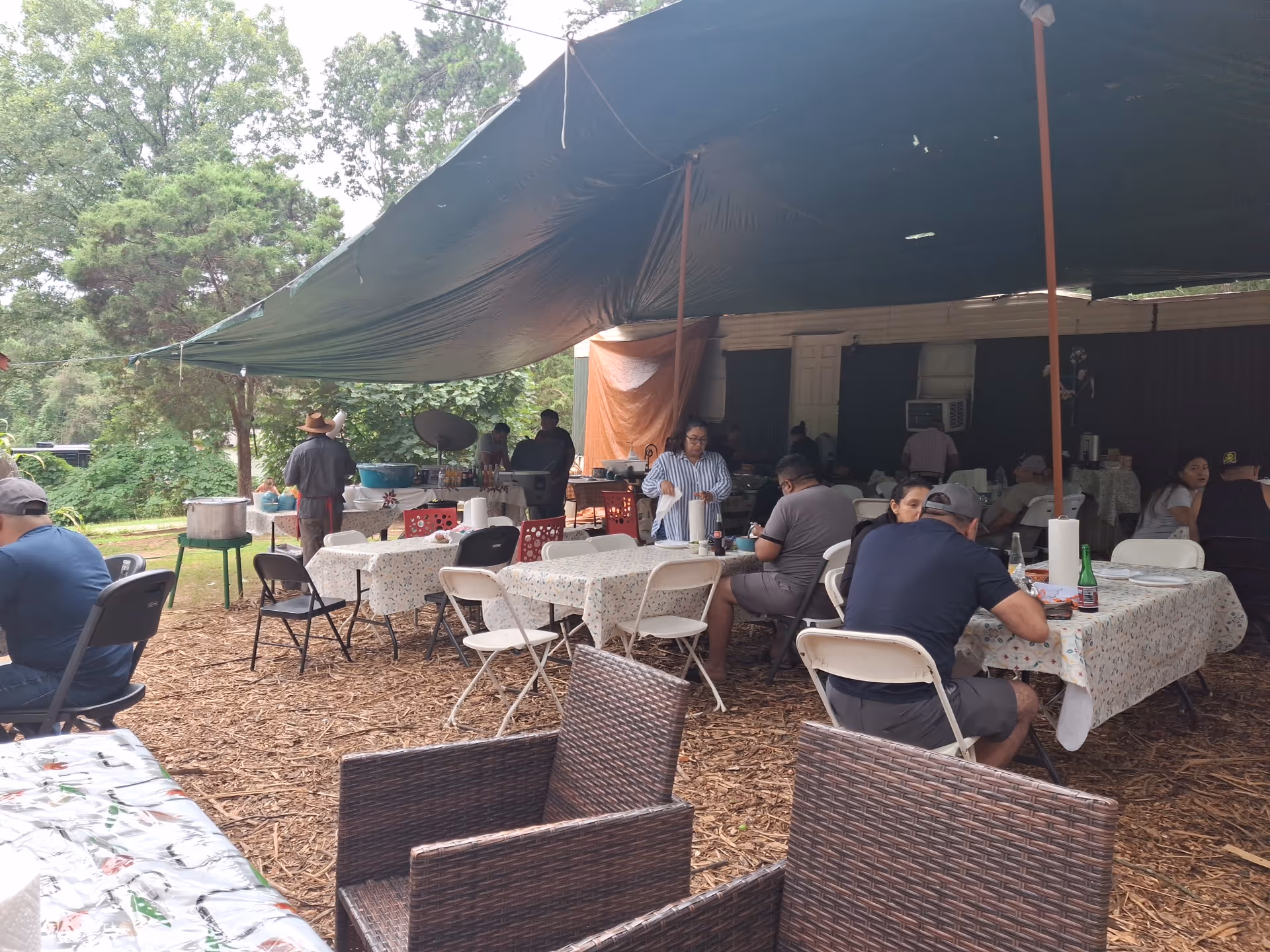 Outdoor covered dining area with tables, chairs, and residents seated under a large canopy.