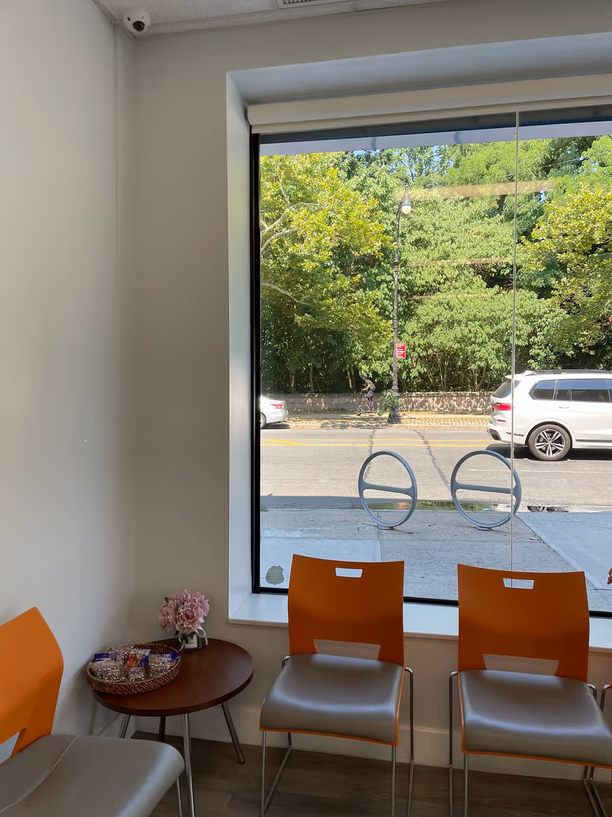 Interior waiting area with orange chairs, a small table, flowers, and snacks by a large window.