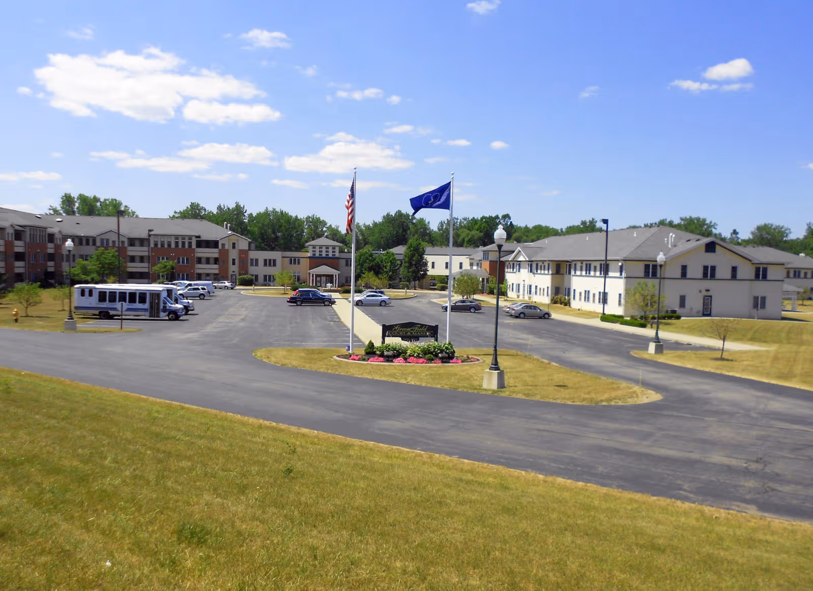 Wide view of GreenField Court senior living campus with circular driveway and flags