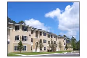 Three-story beige senior living building with arched entrance and manicured lawn under blue sky.