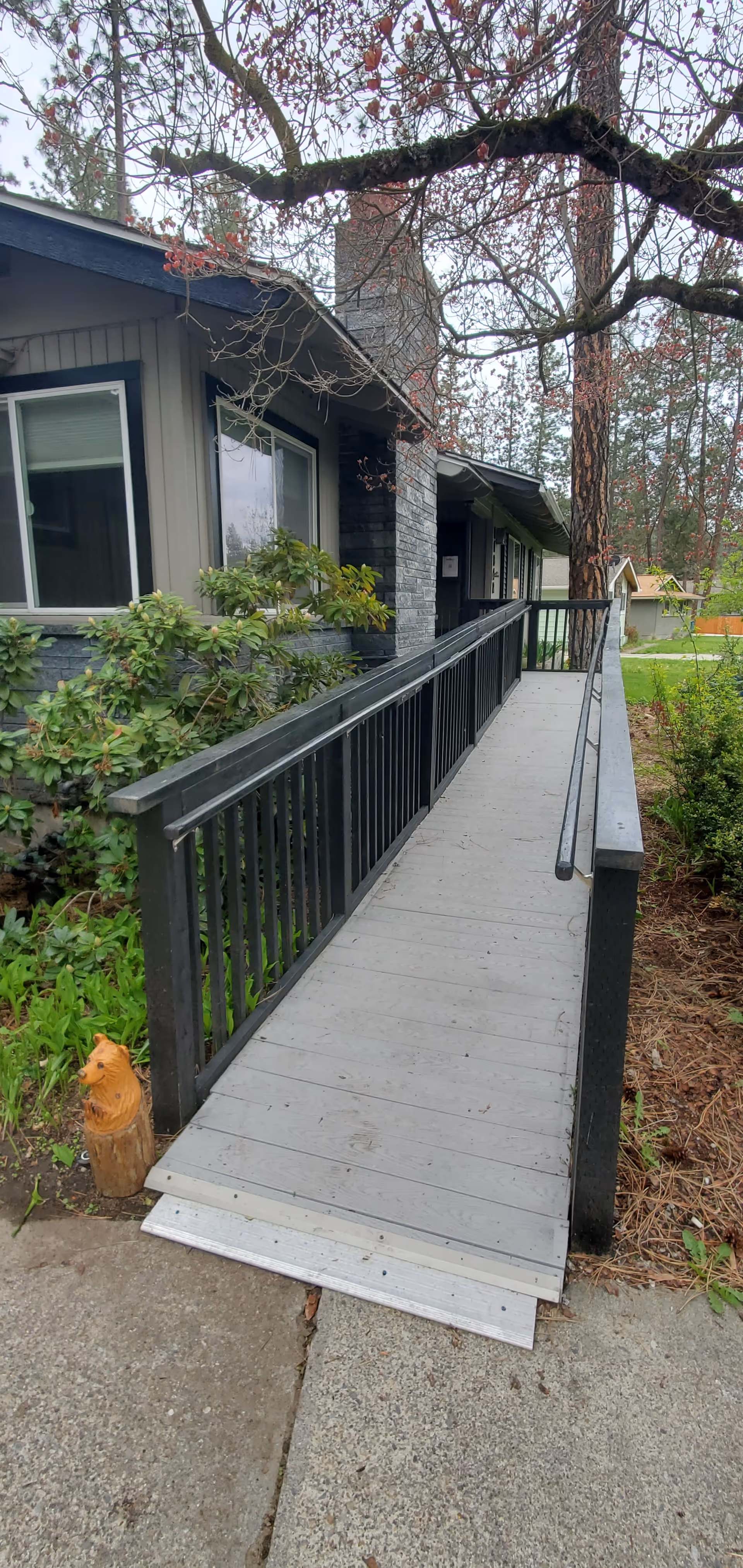 Ramp leads to the entrance of a grey residential facility with greenery along the walkway.