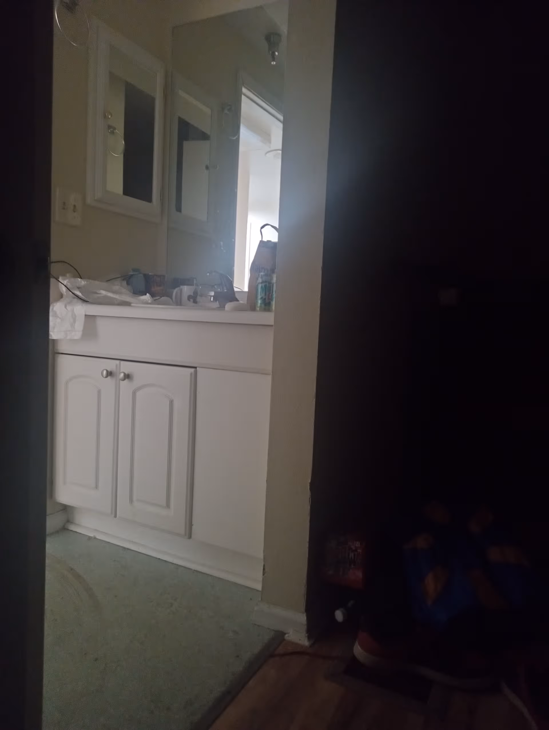 White bathroom vanity with sink, mirror, and clutter on the counter.