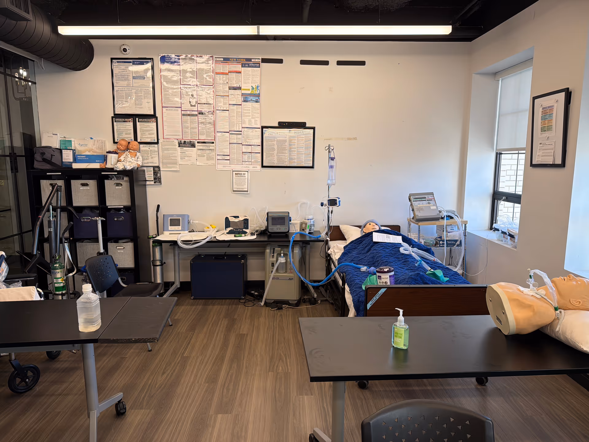 Simulation hospital room with a patient bed, mannequins, and monitoring equipment.