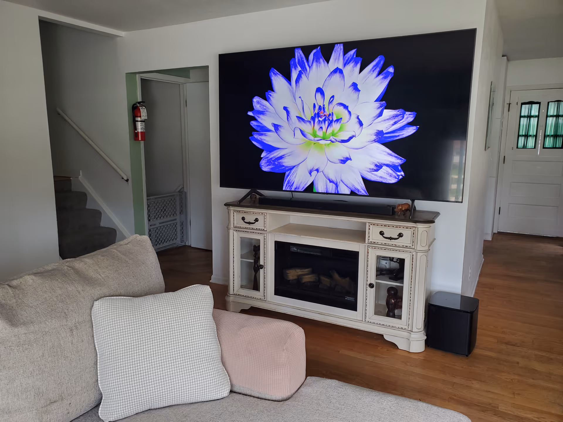 Living room with a large TV on a white console, a sofa, and hardwood floors.