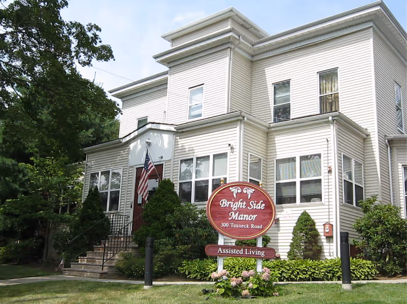 White two-story assisted living building with Bright Side Manor sign and landscaped front entrance.