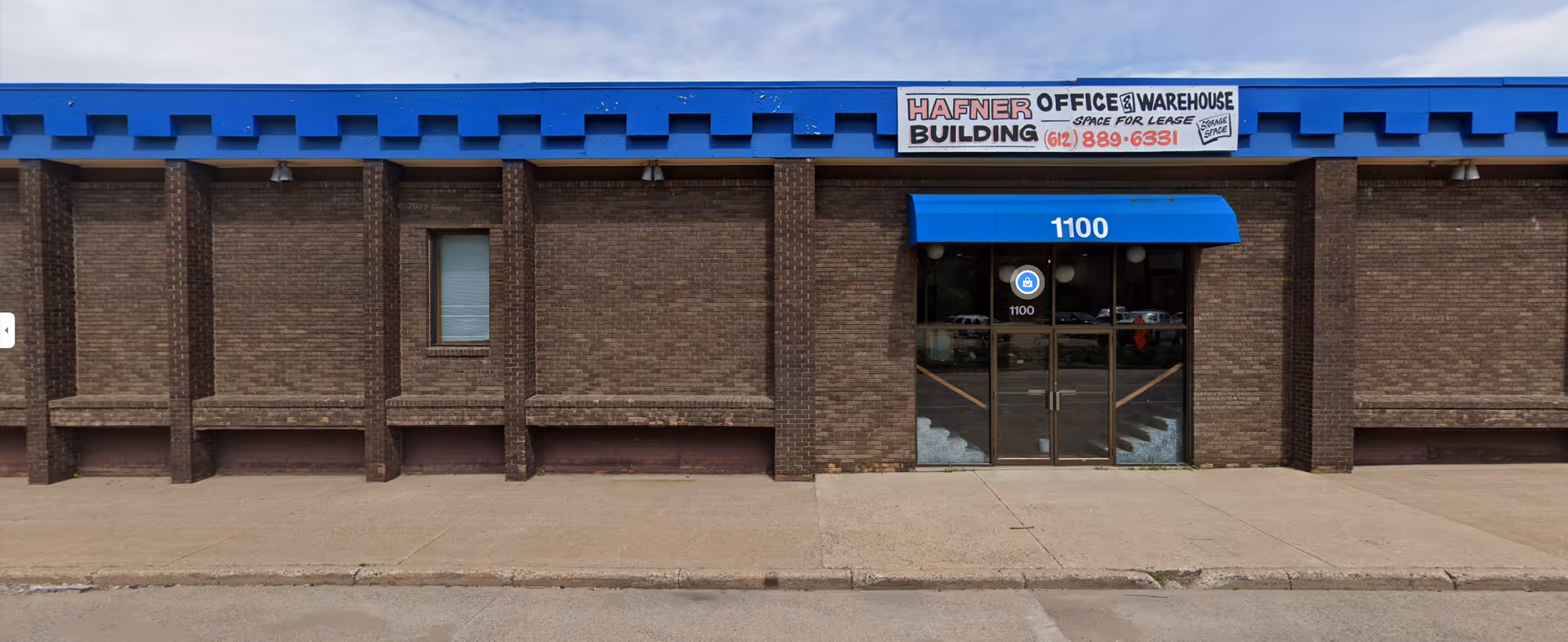 Brick storefront exterior with blue awning and glass entrance door.