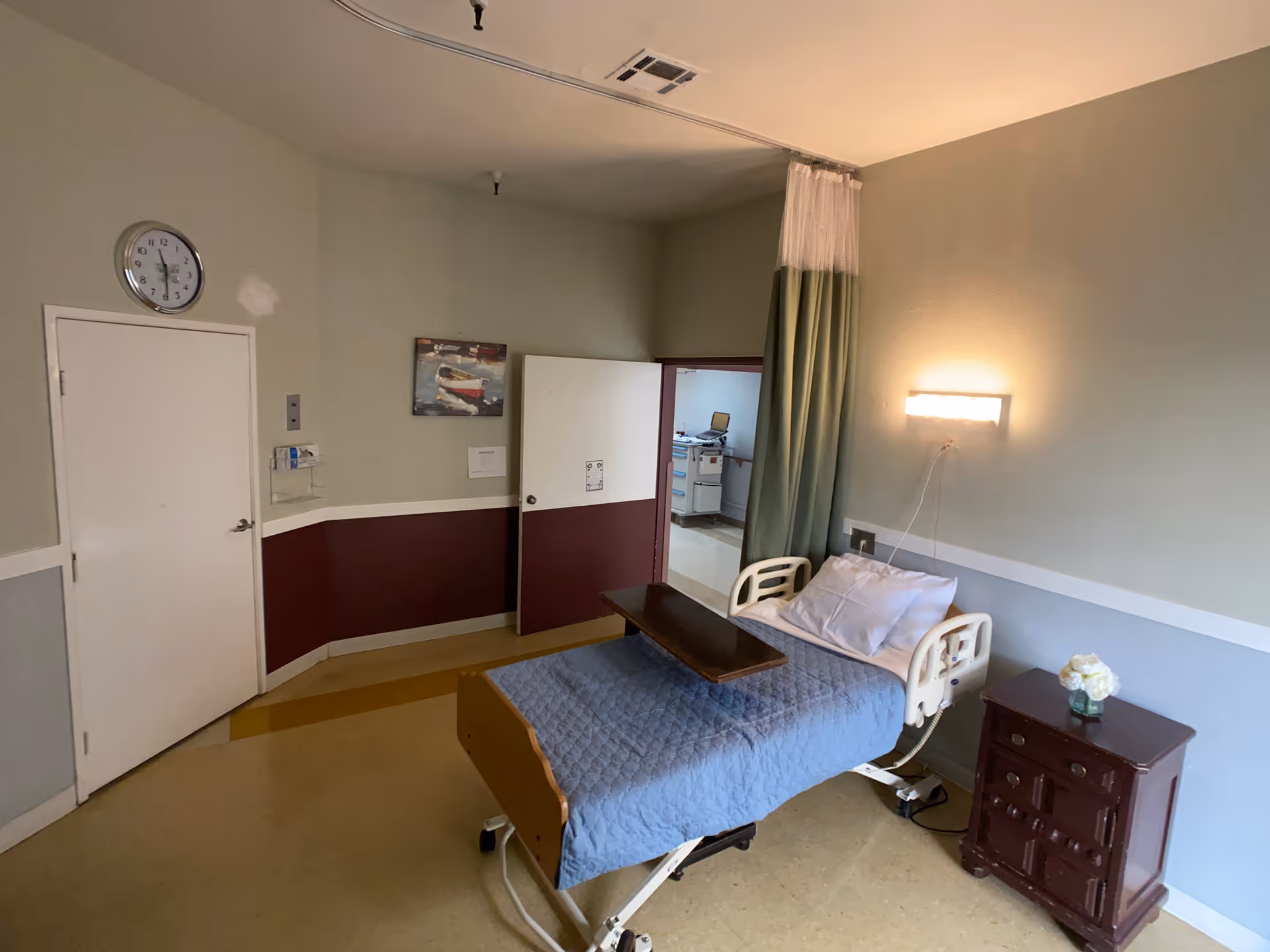 Hospital-style patient room featuring a bed, side table, and privacy curtain.