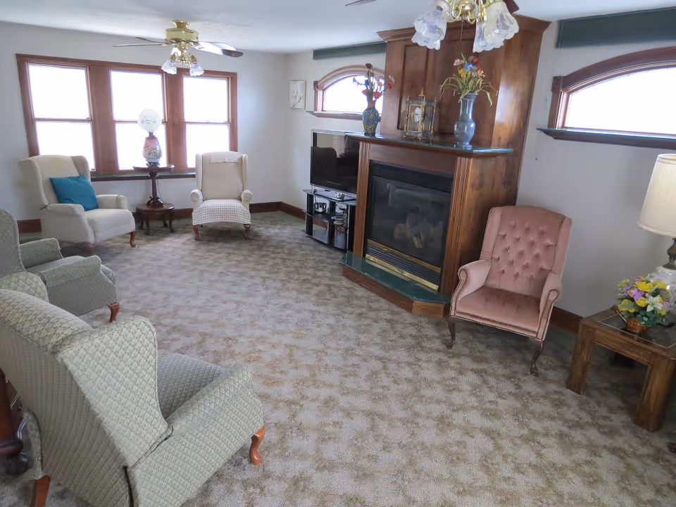 Cozy living room with fireplace, soft chairs, and a TV in a senior facility.