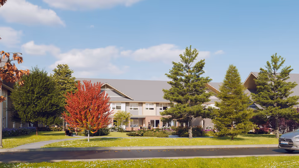 Front exterior of a two-story senior living building with manicured lawn, trees and a driveway under a blue sky.
