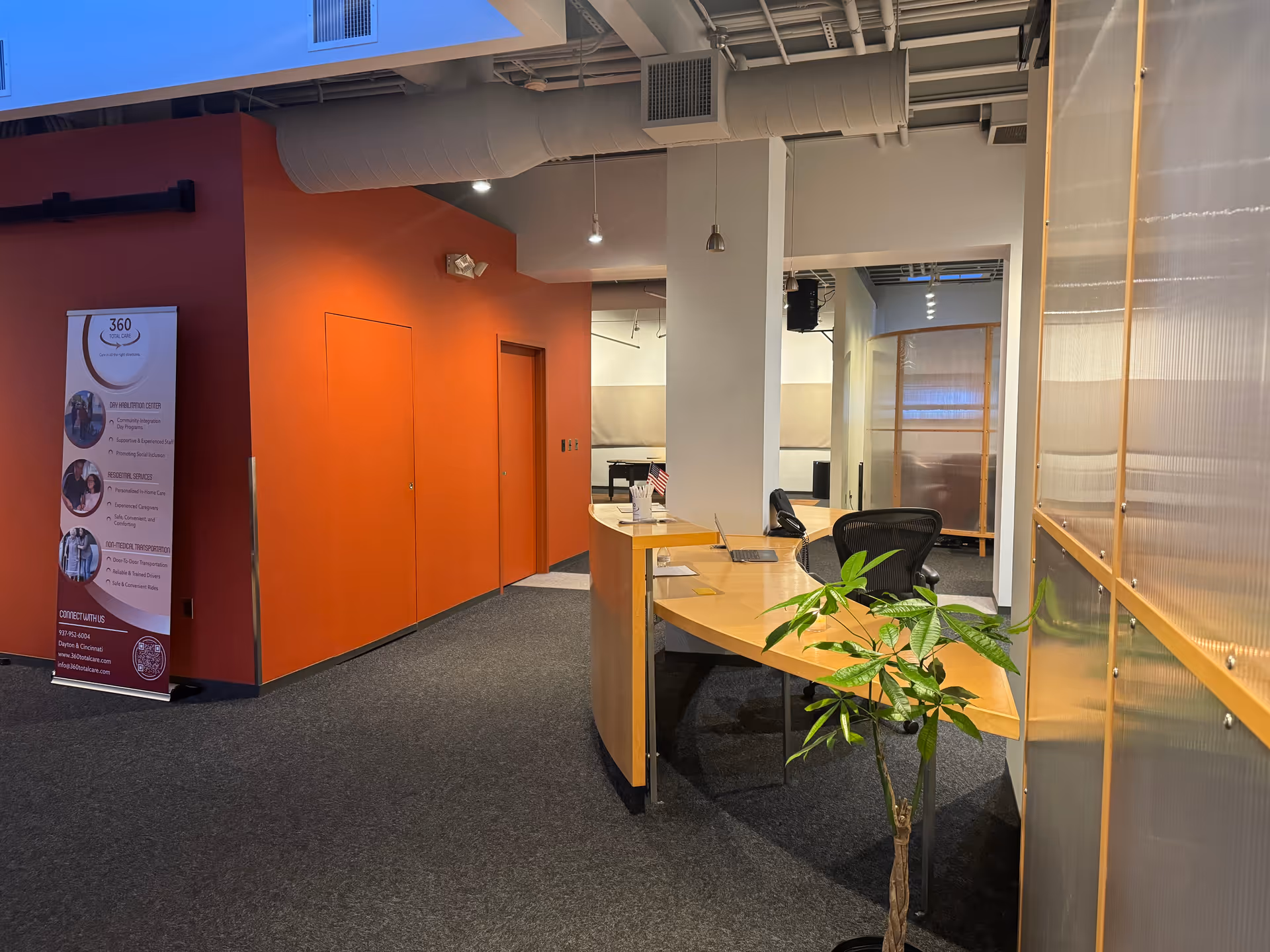 Interior office reception area with an orange wall, curved desk, banner, and plant.