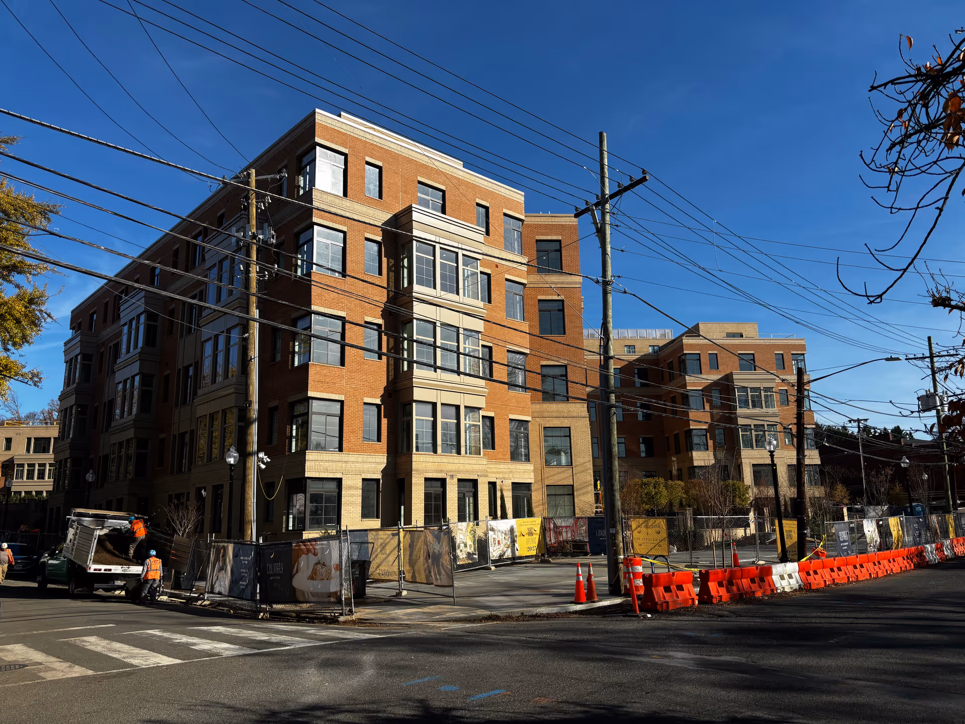 A multi-story brick senior living building under construction with fencing, traffic cones, and overhead utility wires.