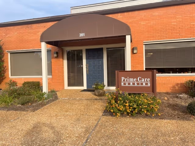 Brick building entrance with blue door under brown arched awning and Prime Care Nursing sign.