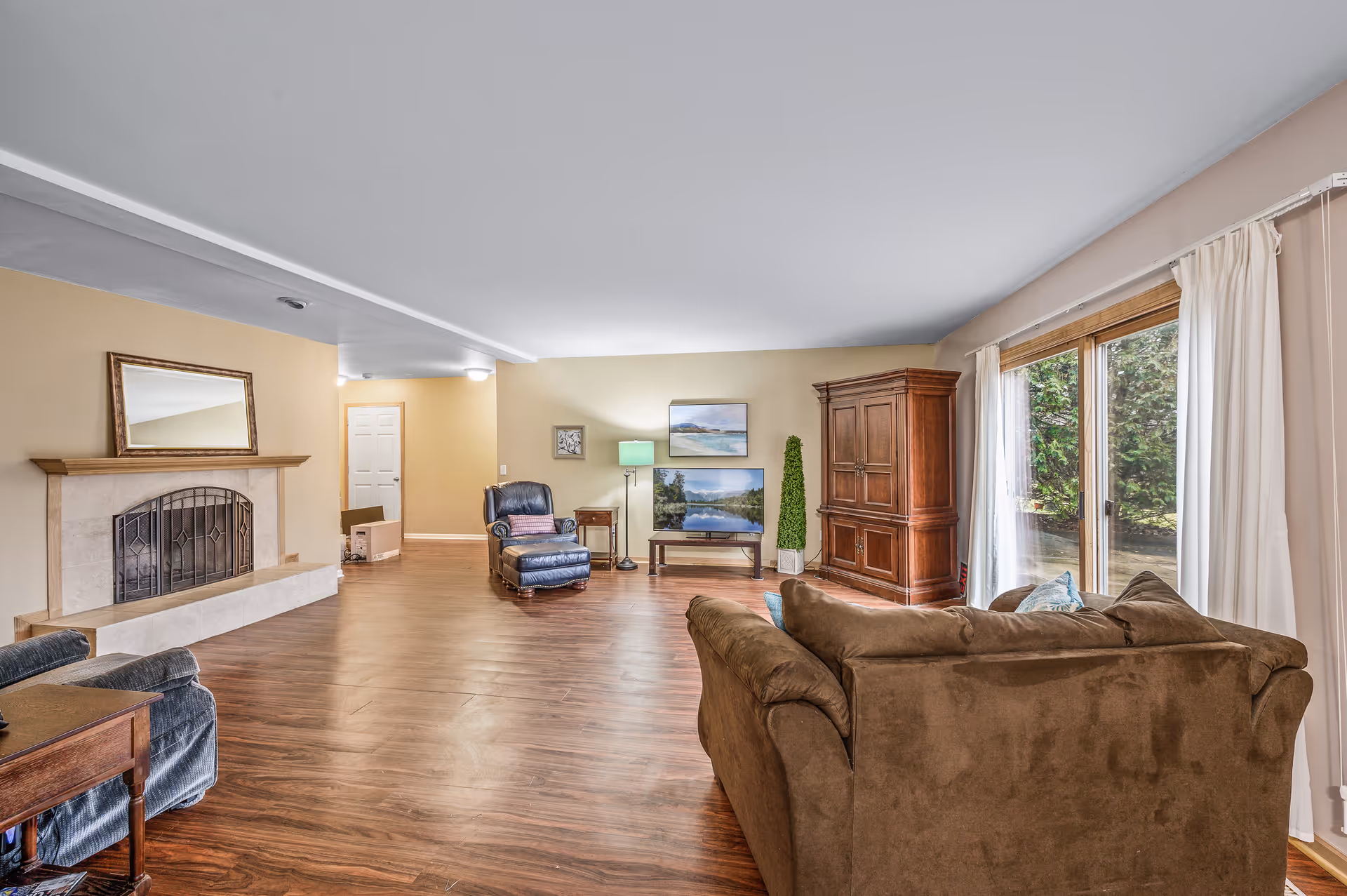Spacious living room with brown sofa, chairs, fireplace, and large sliding glass doors to the outdoors.