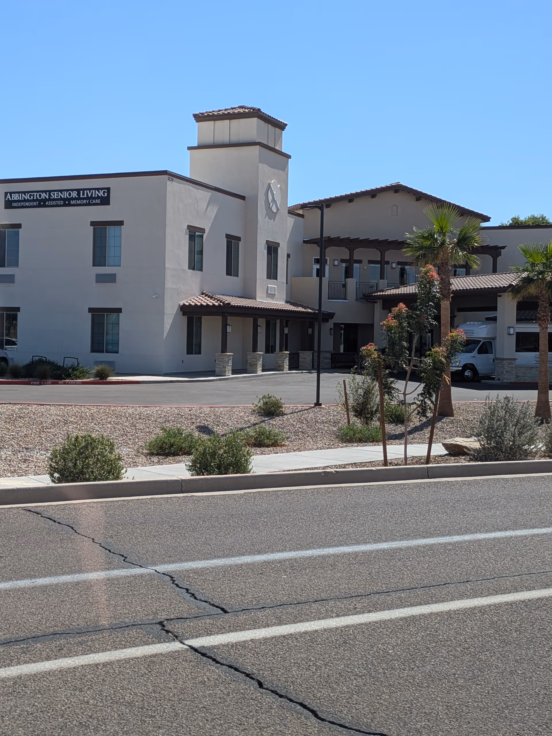 Exterior view of Abbington Senior Living building with sign, palm trees, and driveway.