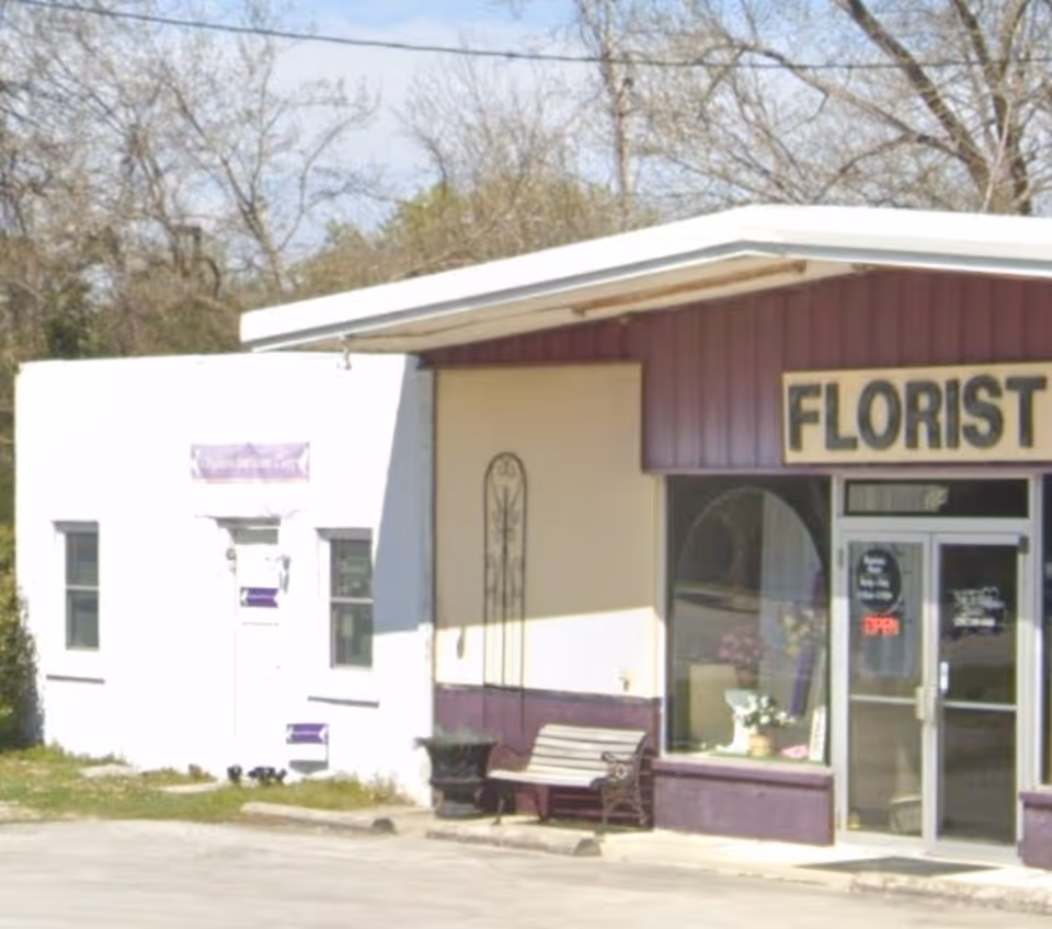 Small storefront with purple trim labeled FLORIST and a bench outside.