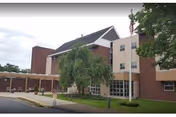 Exterior view of a brick and beige senior living building with trees and a covered entrance.