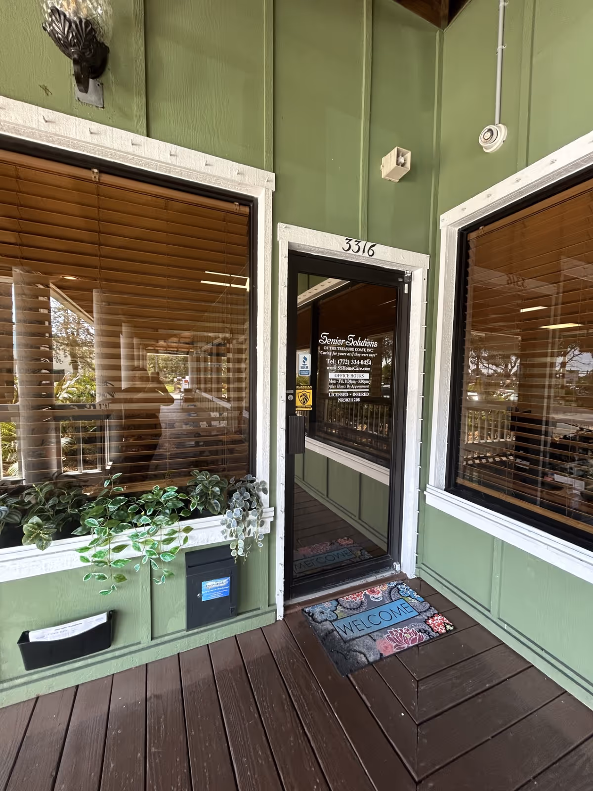 Green exterior entrance of Senior Solutions facility with glass door, windows, and welcome mat.