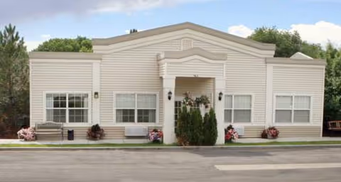 Front exterior of a single-story beige senior living residence with plants and a small entry.
