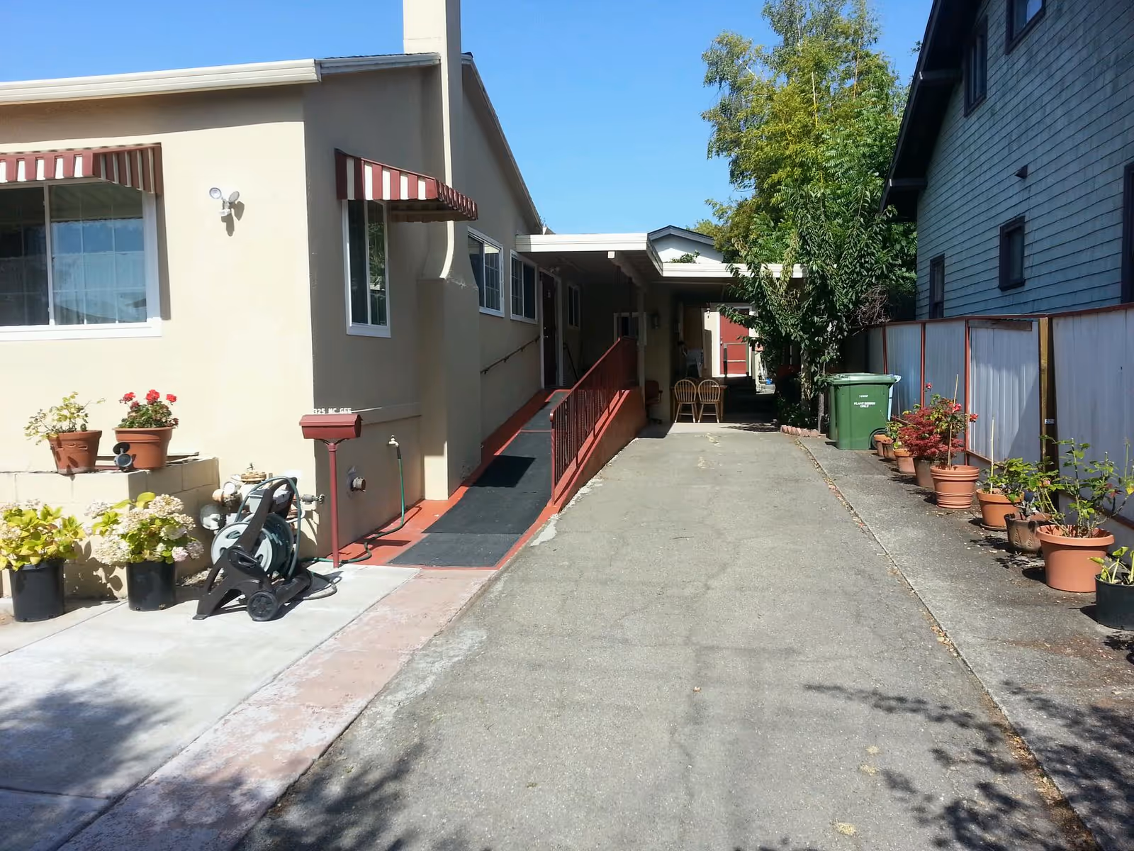 Exterior walkway of a senior living facility with potted plants, ramp, and seating.