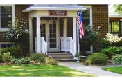 Brick building entrance with white porch railing, steps, American flag, and surrounding greenery.