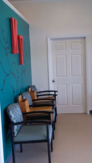 Row of chairs along teal-walled hallway with a white door.