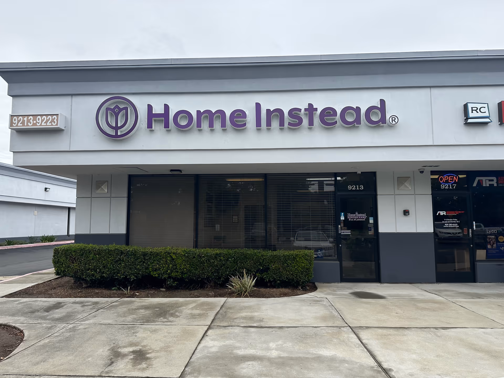 Front exterior of a storefront with a large purple Home Instead sign and glass doors.