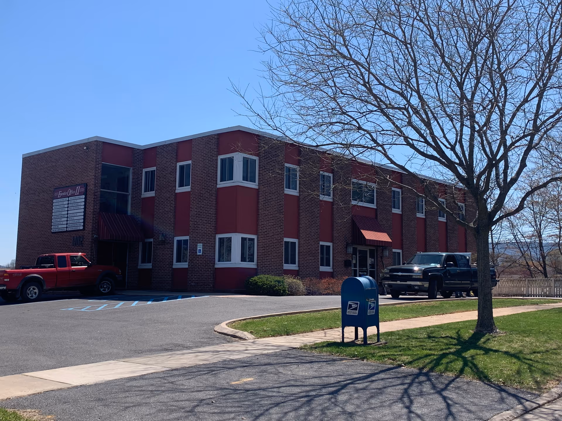 A brick, two-story senior living facility exterior with parked trucks and a blue mailbox.