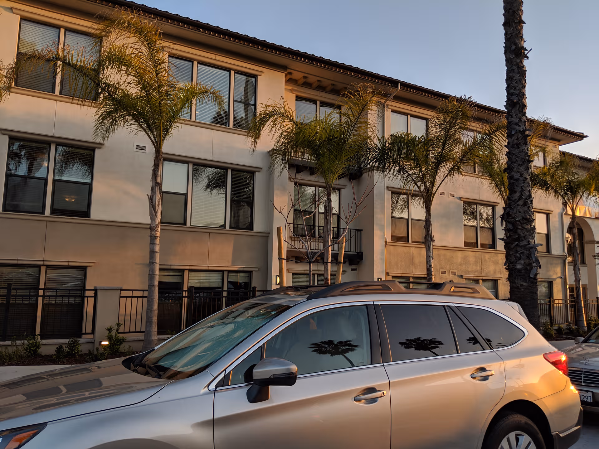 Exterior view of a multi-story senior living building with palm trees and a parked car.