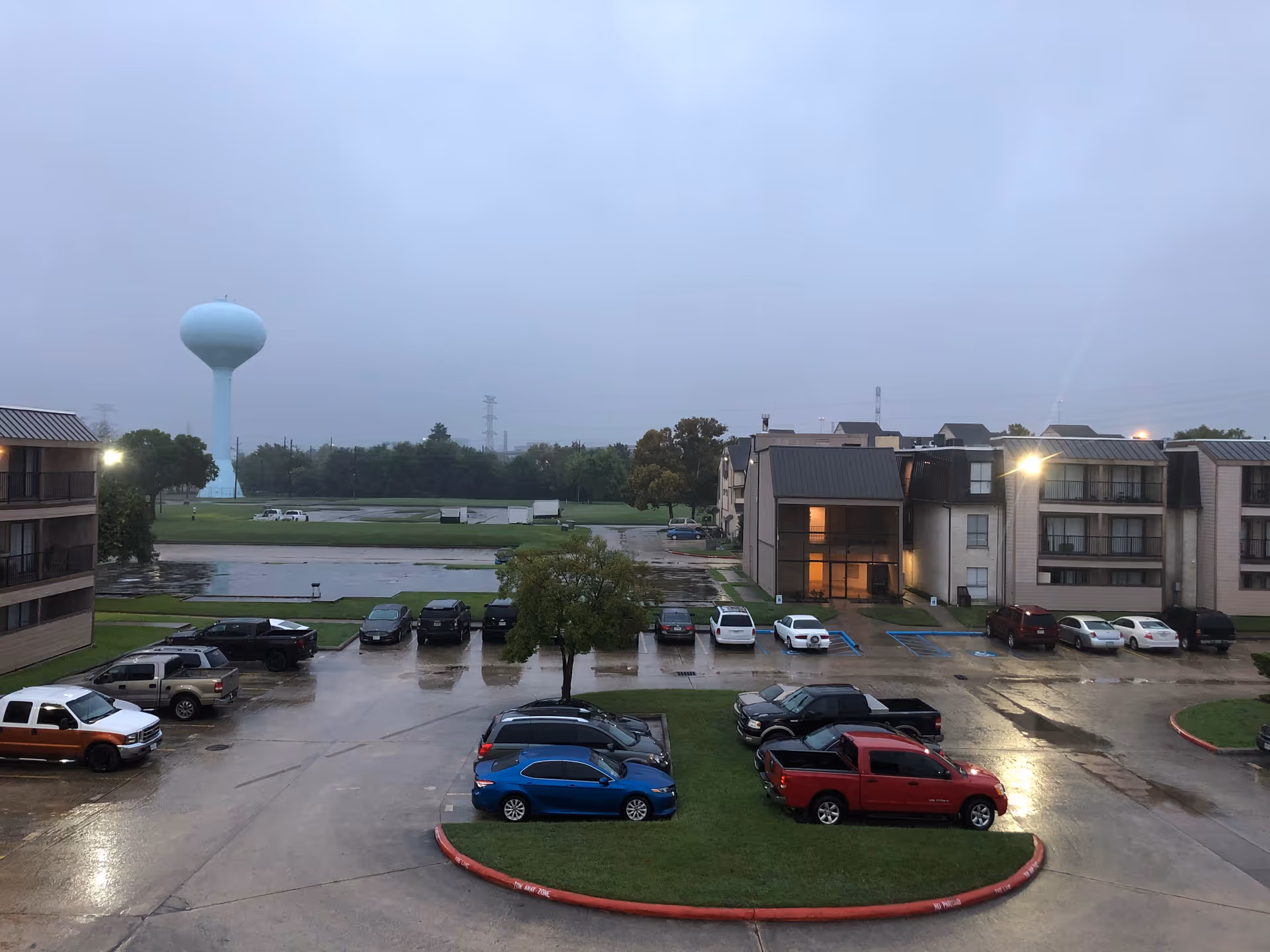 Overcast exterior view of a senior housing complex with parking and a distant water tower.
