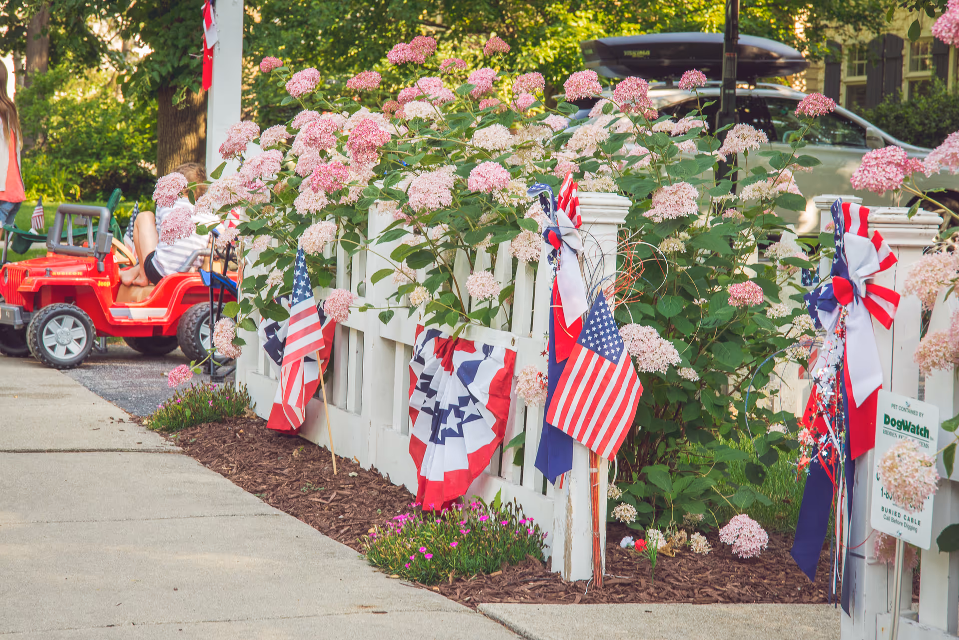 Front walkway with white fence, pink hydrangeas, and patriotic American flags.