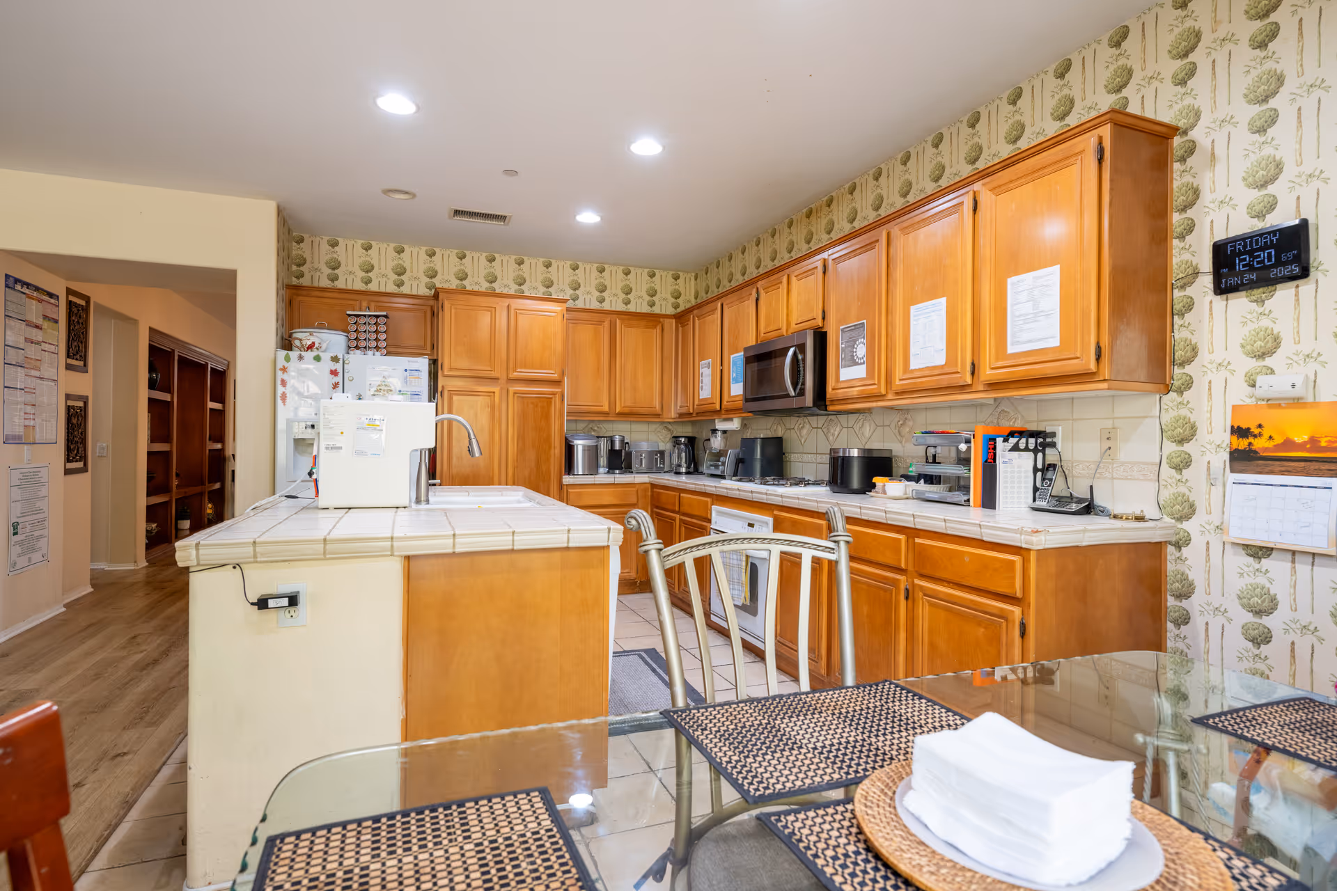 Bright communal kitchen with wooden cabinets, island, and a glass dining table.