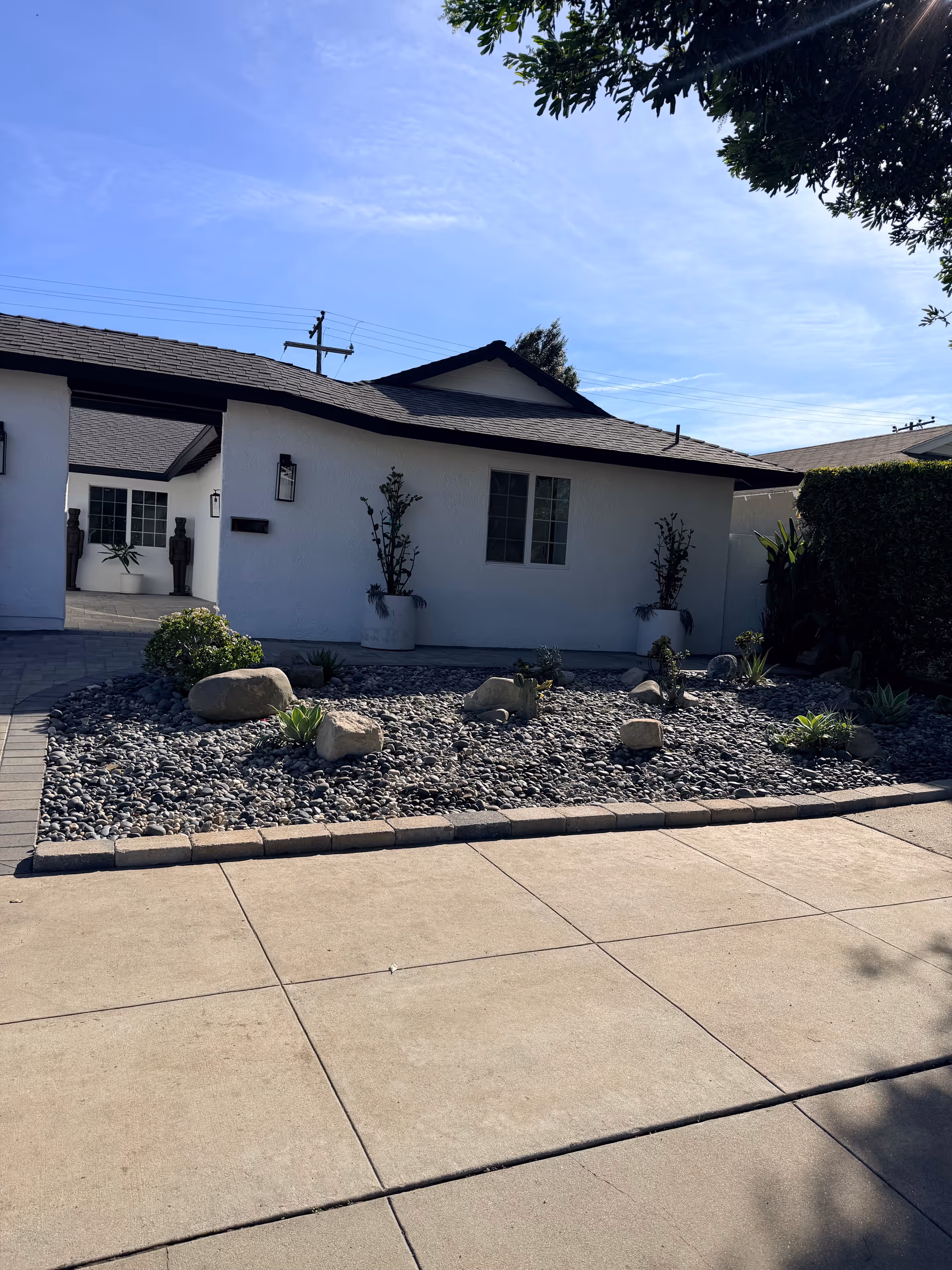White single-story Encanto Living building with a rock garden and paved front driveway.