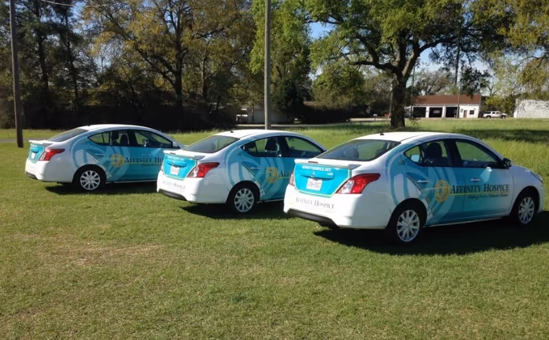 Three Affinity Hospice branded cars parked on a grassy field near trees.