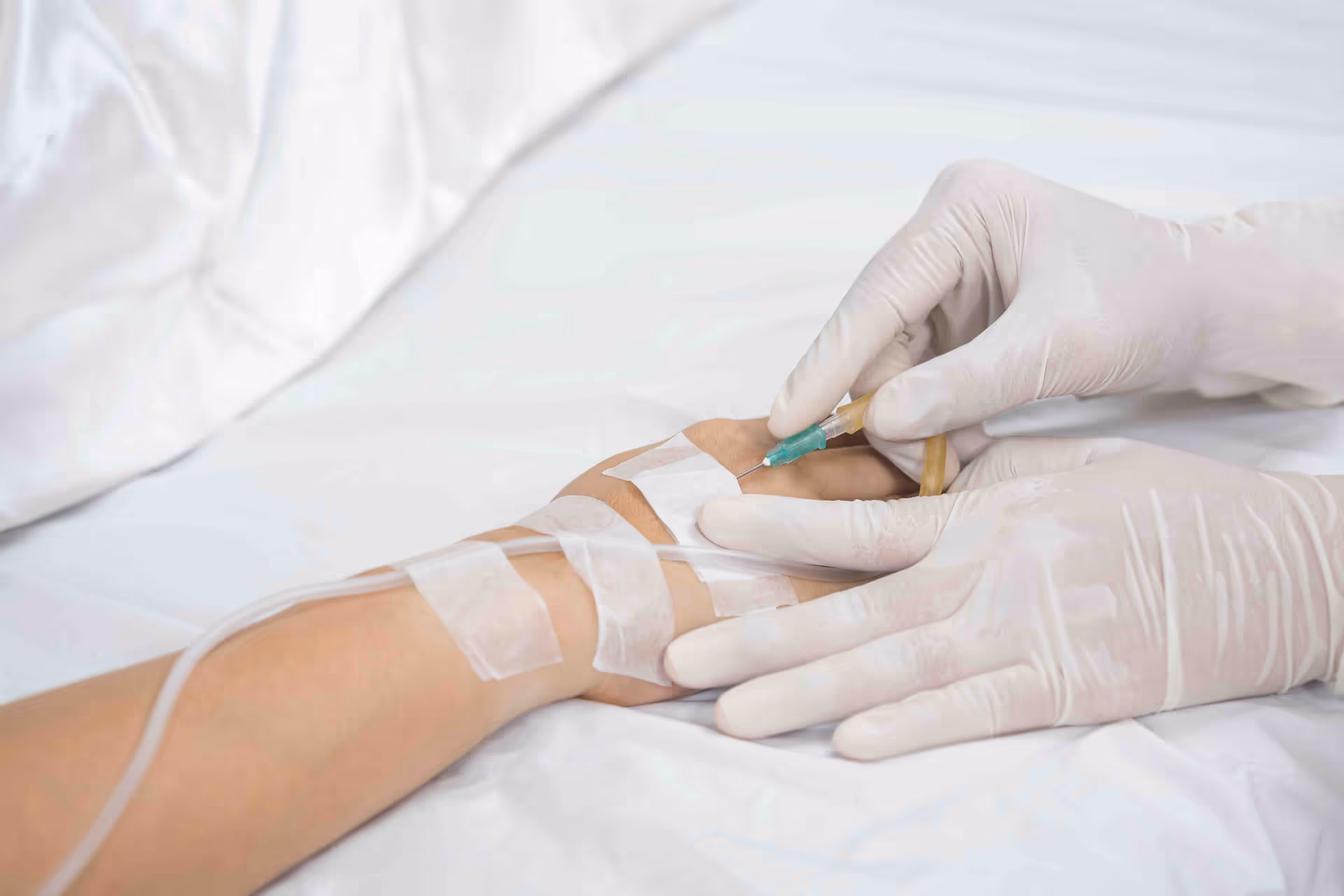 Medical care provider inserts IV into a patient's arm with gloved hands.
