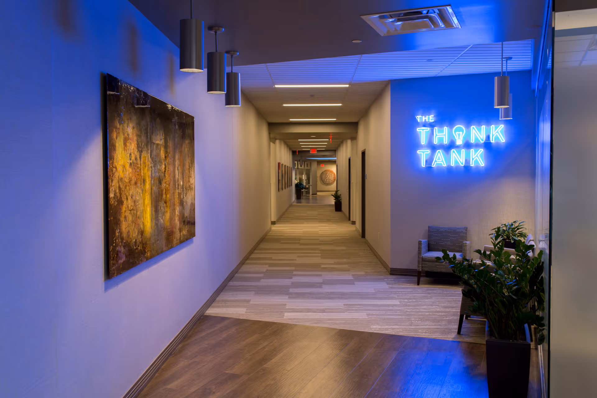 Long modern hallway in a facility with blue neon Think Tank sign and seating.