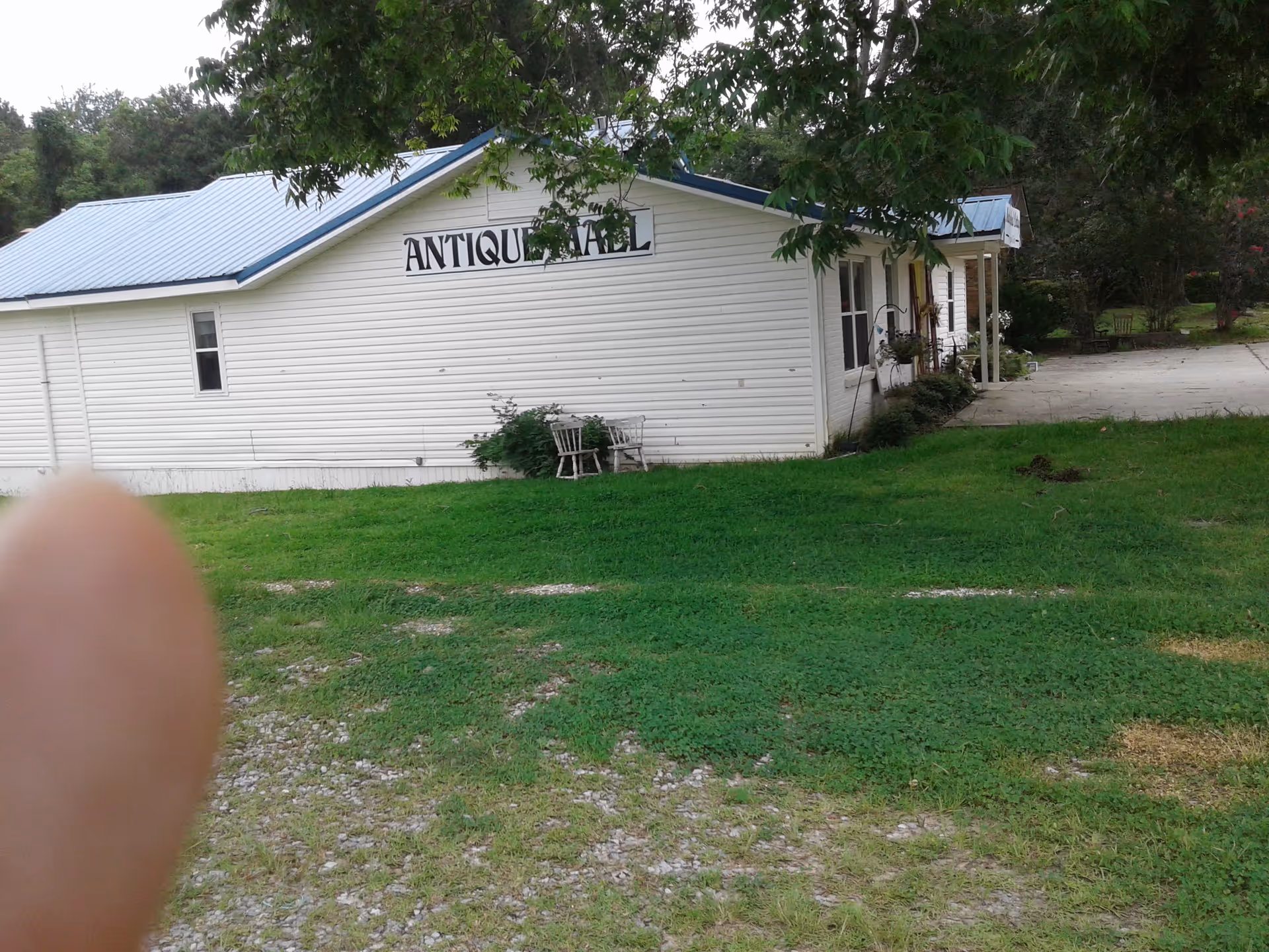 White single-story building labeled Antique Hall sits on a grassy lawn with chairs outside.