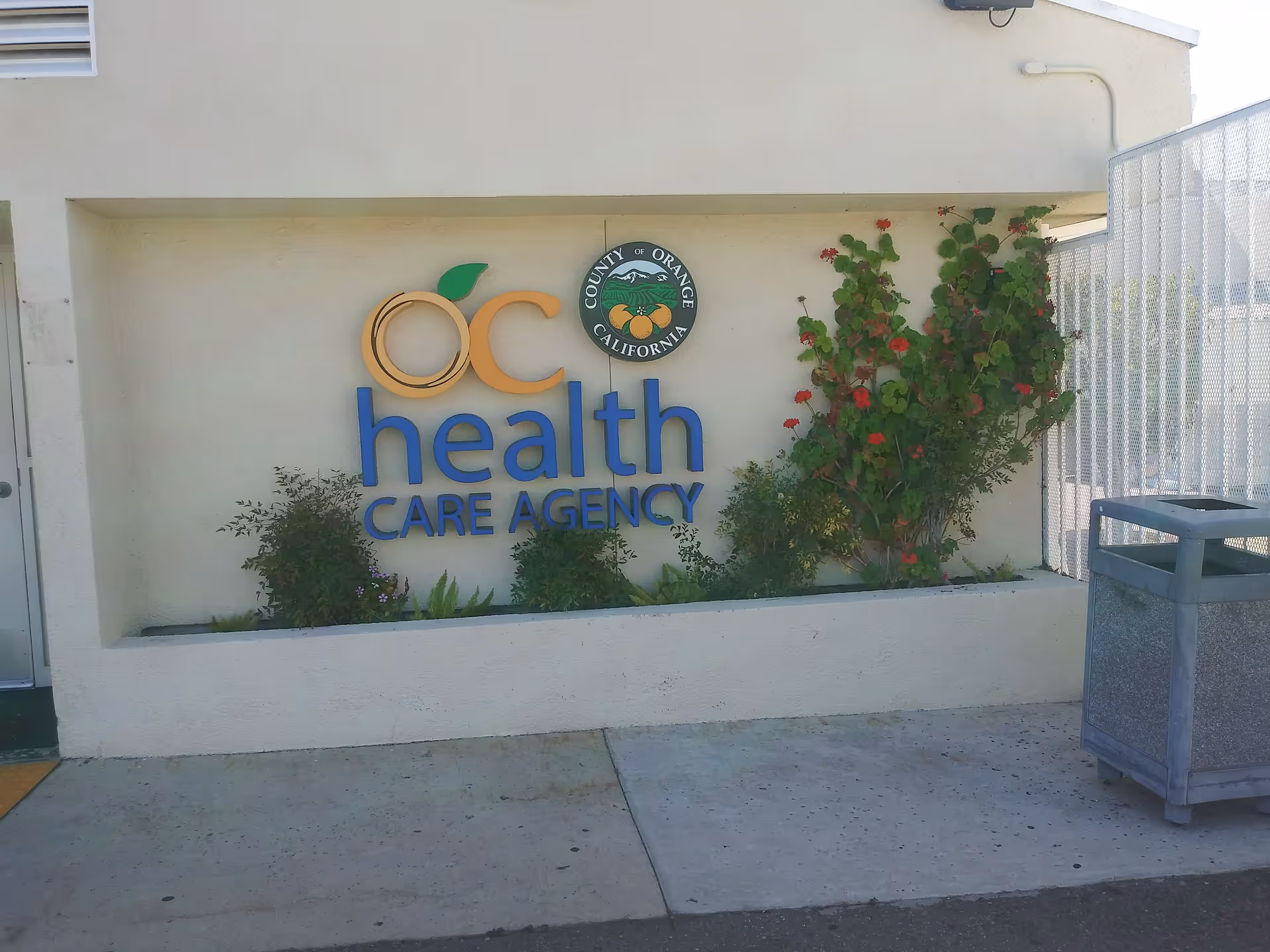 Exterior wall with OC Health Care Agency sign and surrounding greenery