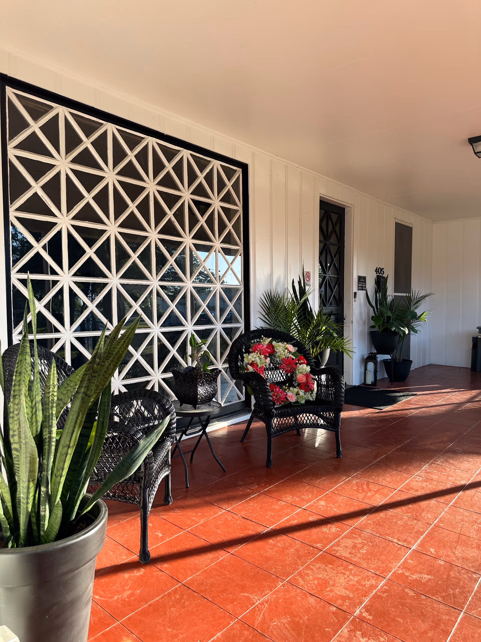 Covered porch with wicker chairs, potted plants, and a lattice window wall at the entrance.
