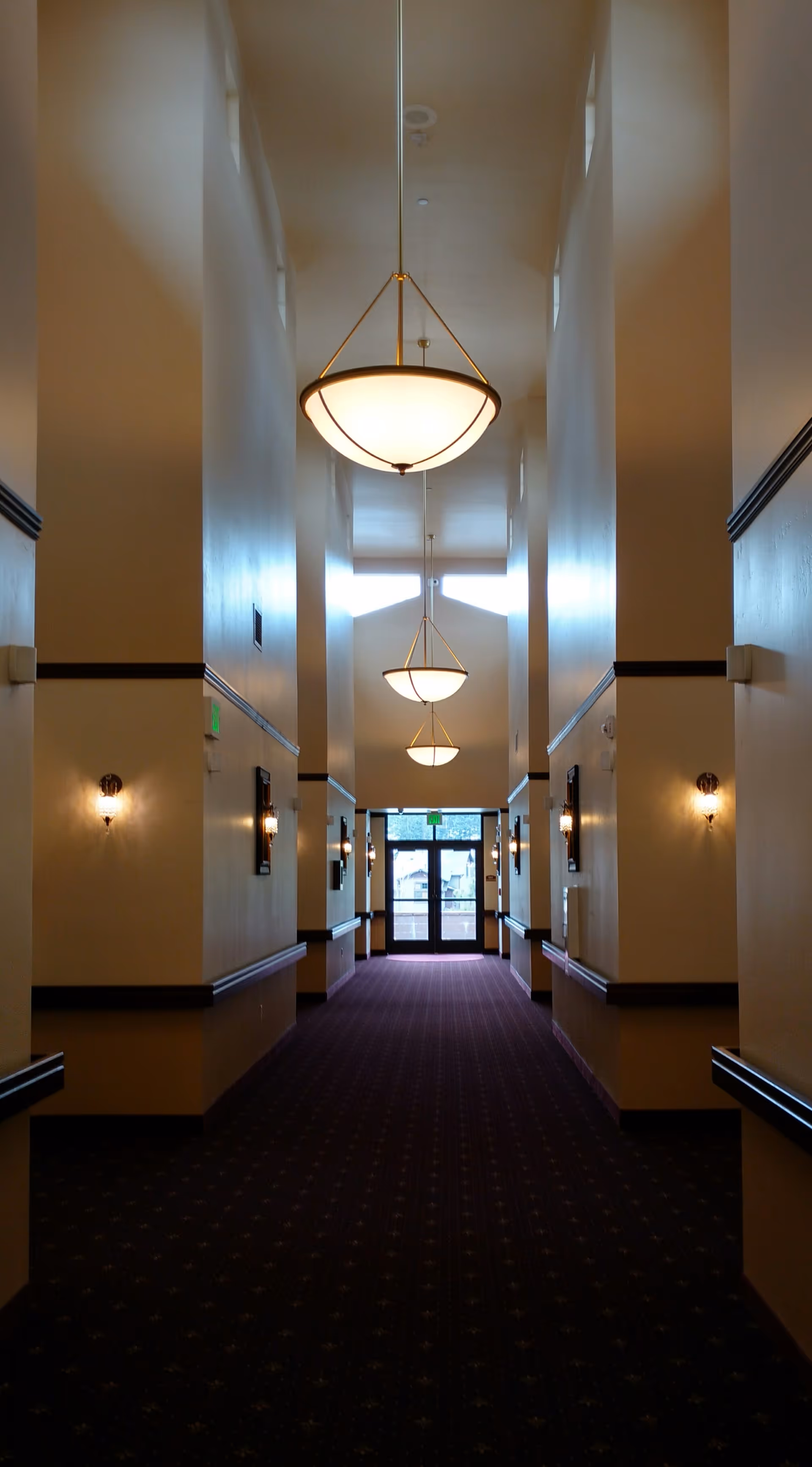 Long, well-lit hallway in a senior living facility with hanging pendant lights.