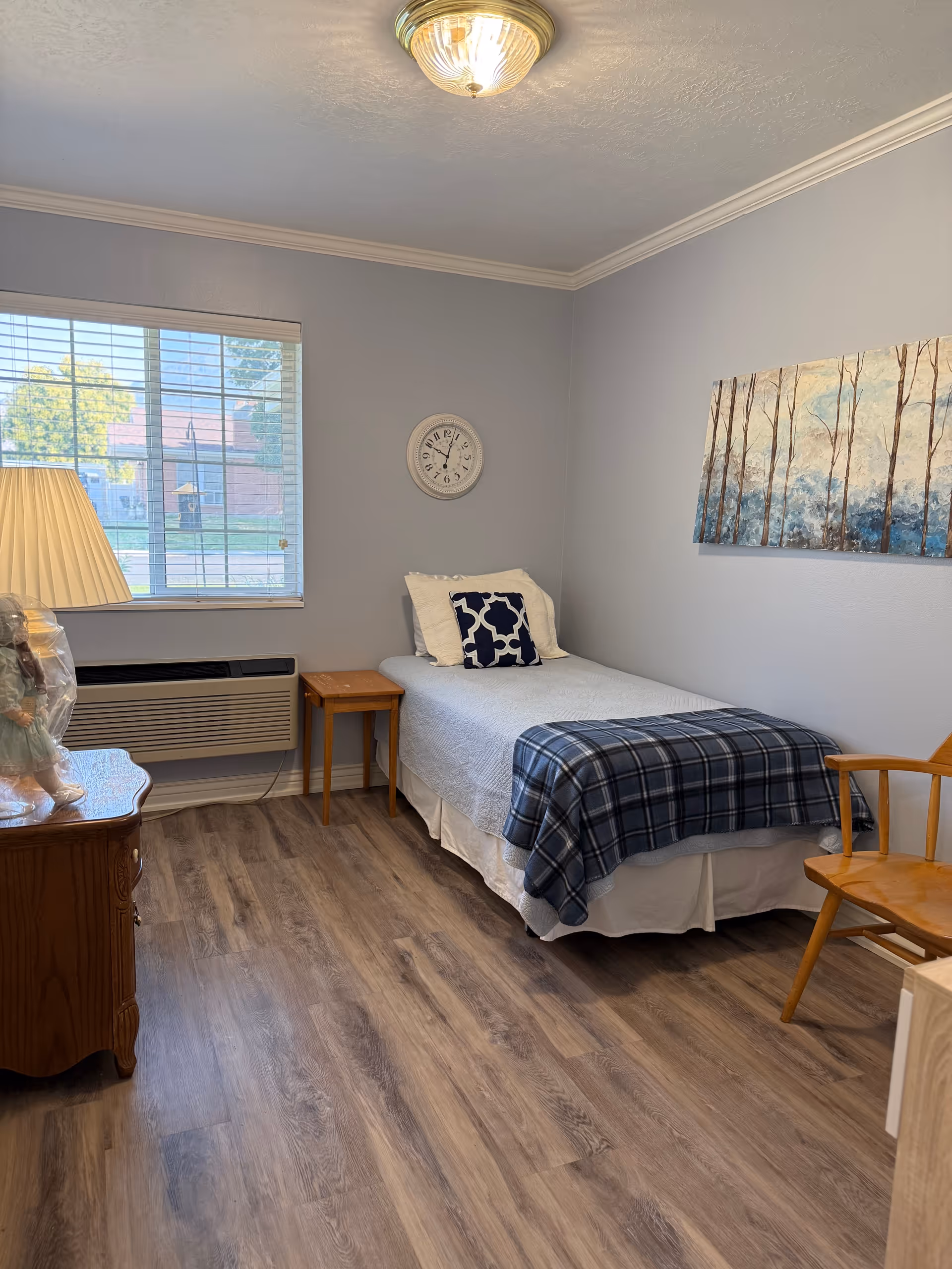 Cozy bedroom with a single bed, plaid blanket, side table, lamp, and wall art.