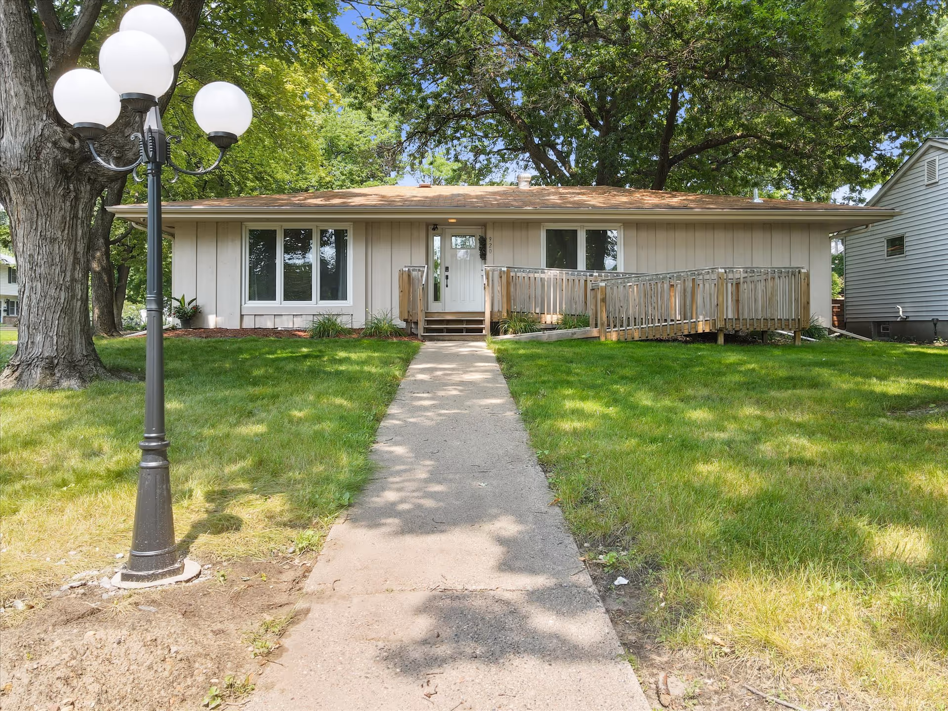 A single-story beige senior living facility with ramp and walkway, lamp post, and green lawn.