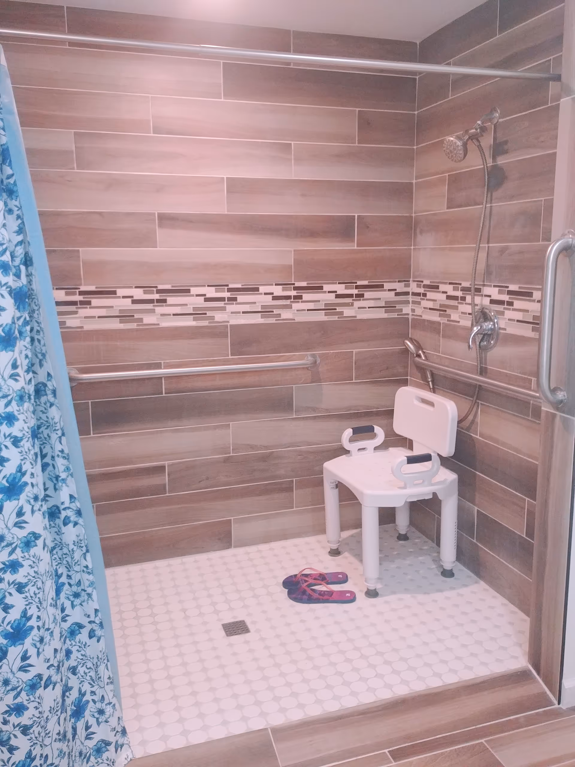 Accessible bathroom featuring a shower chair, grab bars, and tiled walls.